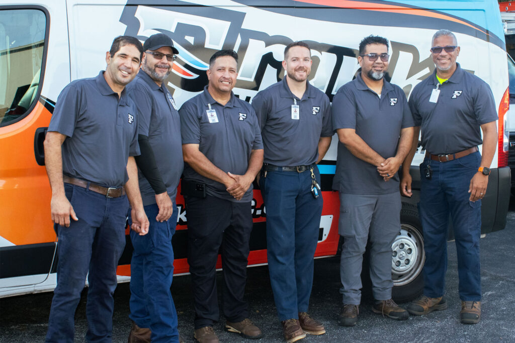 Six air conditioning repair technicians smiling next a van/