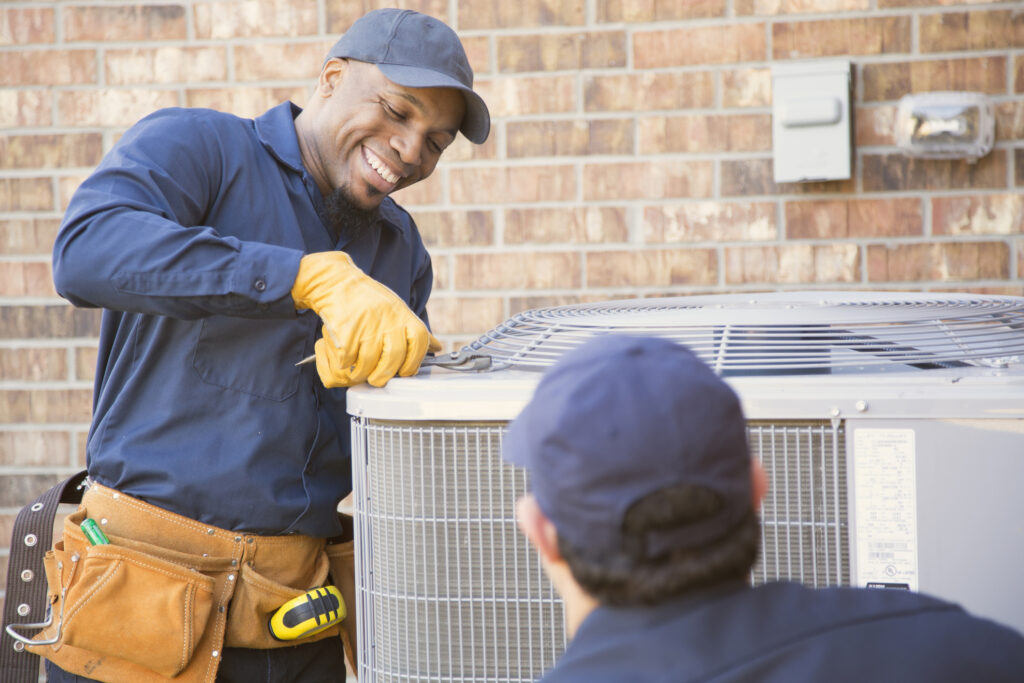 Multi Ethnic Team Of Blue Collar Air Conditioner Repairmen At Work.